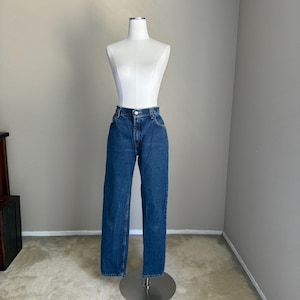 May include: A pair of high-waisted blue denim jeans featuring a classic straight-leg cut, a button and zipper fly closure, and traditional five-pocket styling. The fabric has a medium-wash finish with subtle fading along the thighs and knees.
