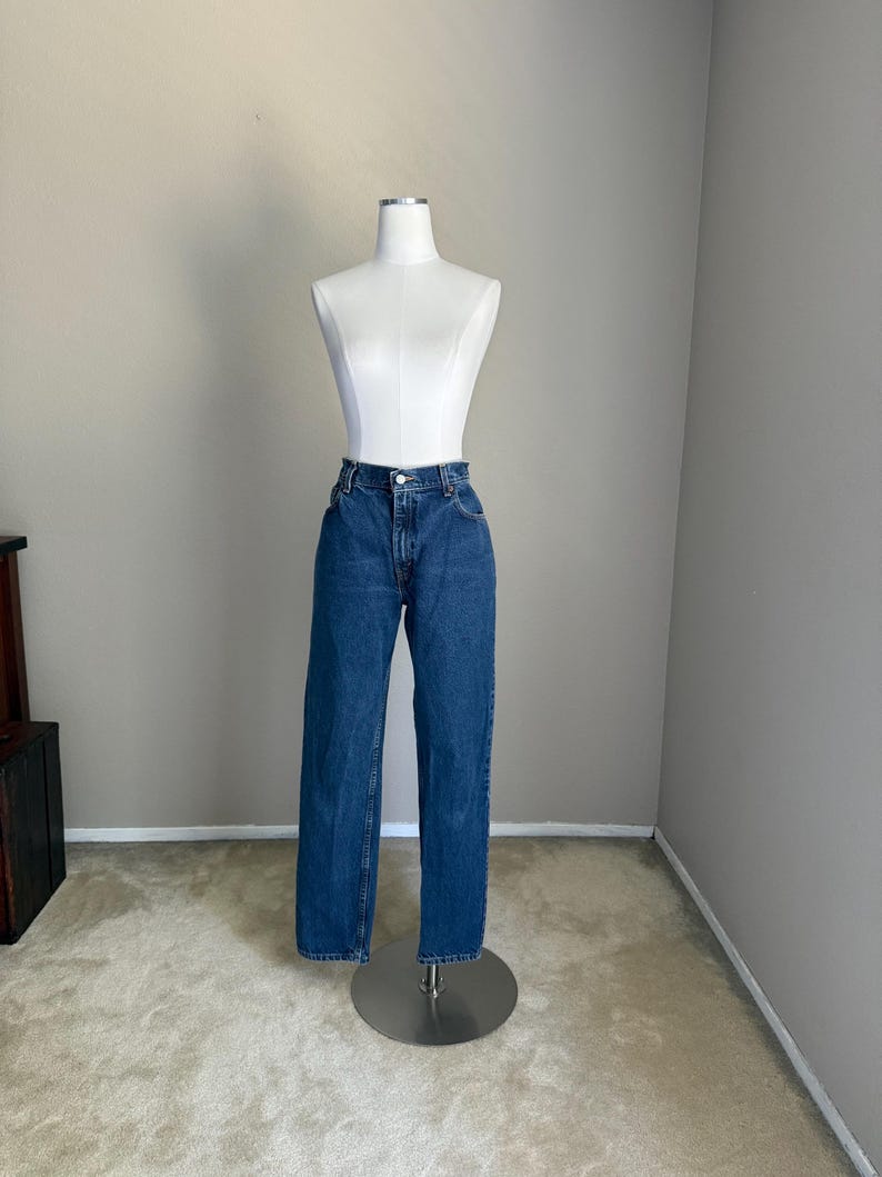 May include: A pair of high-waisted blue denim jeans featuring a classic straight-leg cut, a button and zipper fly closure, and traditional five-pocket styling. The fabric has a medium-wash finish with subtle fading along the thighs and knees.