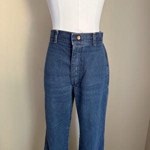 K&ouml;nnte beinhalten: Dunkelblaue Jeans mit hoher Taille und ausgestellten Beinen. Die Jeans haben einen Knopfverschluss und ein klassisches F&uuml;nf-Taschen-Design. Die Jeans werden auf einer Schaufensterpuppe pr&auml;sentiert.