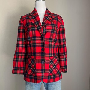 May include: A red plaid blazer with navy and green accents. The blazer has two front pockets and two navy buttons. The jacket is displayed on a mannequin with light blue jeans.