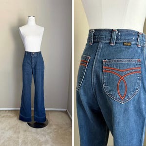K&ouml;nnte beinhalten: Blaue Wrangler Jeans aus Denim mit hoher Taille und ausgestellten Beinen. Die Ges&auml;&szlig;taschen haben ein orangefarbenes Nahtdesign. Die Jeans werden auf einer Schaufeniquin pr&auml;sentiert.