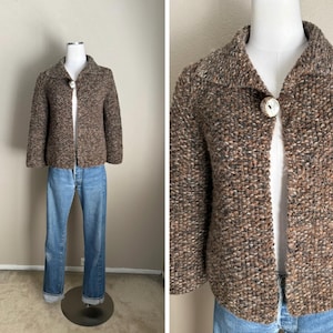 May include: A brown tweed jacket with a large collar and a single, round button closure. The jacket is displayed on a mannequin with blue jeans. The jacket's texture is visible, showcasing a mix of brown and neutral tones.