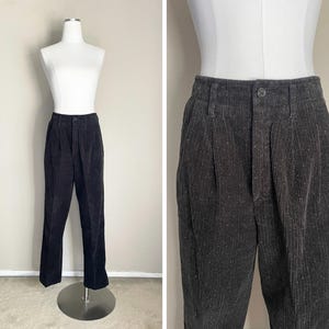 May include: Dark gray corduroy pants with a button closure and pleats. The pants are displayed on a mannequin. The corduroy fabric has a subtle speckled texture, and the pants have a classic, tailored fit.