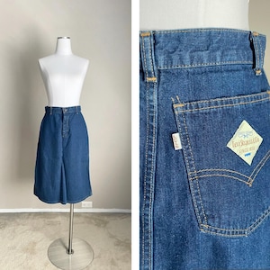 May include: A dark blue denim skirt with a high waist and a straight cut. The skirt has a button closure and a zipper fly. The back pocket has a Levi's patch with the text "Levi Strauss & Co. Since 1853".