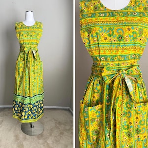 May include: A sleeveless, vintage-style dress in yellow, green, and blue floral patterns. The dress features a fitted bodice, a waist tie, and two front pockets. The skirt has a blue floral border.
