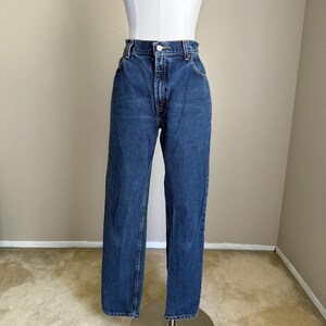 May include: High-waisted blue denim jeans featuring a classic five-pocket design, a metal button closure, and a zipper fly. The jeans have a straight-leg cut with a medium wash finish, visible orange stitching, and belt loops along the waistband.