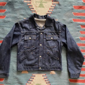 May include: A dark blue denim jacket with a button-up front and two chest pockets. The jacket has a classic style and is made of a sturdy material.