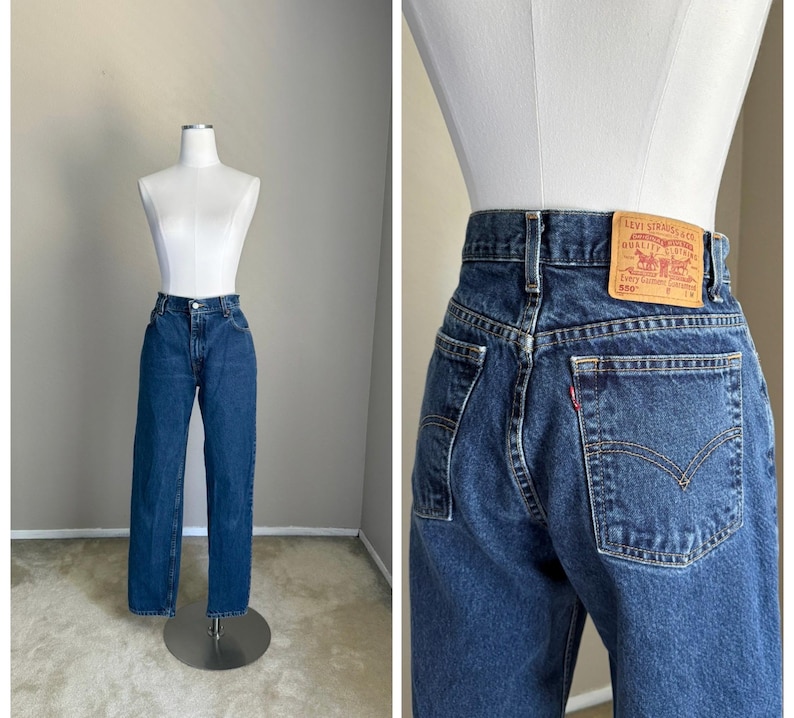 May include: Dark blue denim jeans featuring a high-waisted fit, a button and zipper fly closure, and belt loops. The back includes a tan leather-like patch with the text Levi Strauss & Co. Quality Clothing 550 and a small red brand tab.