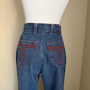 K&ouml;nnte beinhalten: Blaue Jeans mit roten Ziern&auml;hten an den Ges&auml;&szlig;taschen und am Bund. Die Jeans haben ein klassisches, hoch tailliertes Design mit geradem Bein. Die Ges&auml;&szlig;taschen haben ein einzigartiges, geschwungenes Nahtdesign.