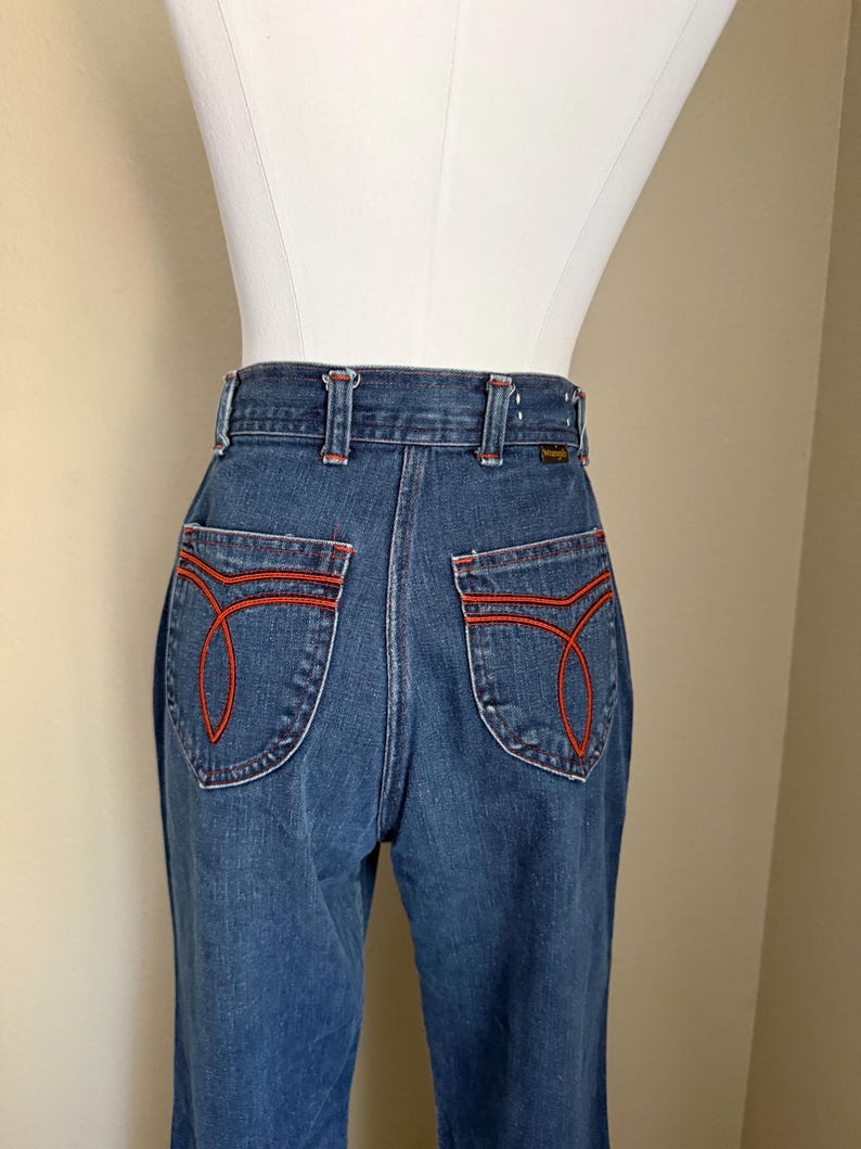 K&ouml;nnte beinhalten: Blaue Jeans mit roten Ziern&auml;hten an den Ges&auml;&szlig;taschen und am Bund. Die Jeans haben ein klassisches, hoch tailliertes Design mit geradem Bein. Die Ges&auml;&szlig;taschen haben ein einzigartiges, geschwungenes Nahtdesign.