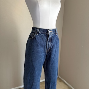 May include: High-waisted blue denim jeans featuring a classic five-pocket design, a metal button closure, and a zip fly. The jeans have a straight-leg cut with visible stitching along the seams and a medium-wash finish on the durable cotton fabric.