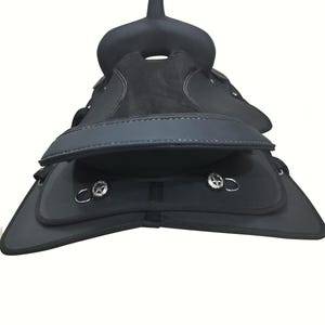 May include: A black horse saddle with a raised pommel and cantle. The saddle features a suede seat and leather flaps with silver-toned hardware. White stitching accents the edges of the saddle.