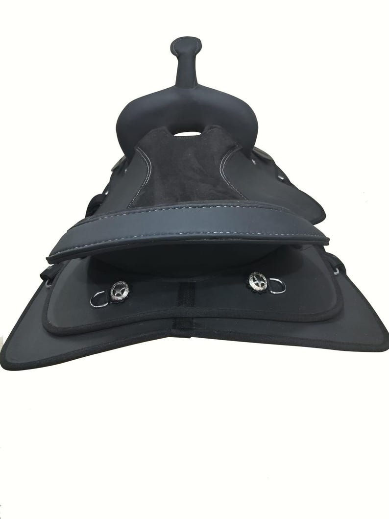 May include: A black horse saddle with a raised pommel and cantle. The saddle features a suede seat and leather flaps with silver-toned hardware. White stitching accents the edges of the saddle.