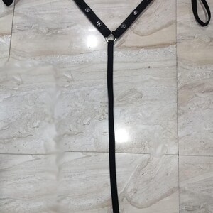 May include: Black harness with silver-tone metal hardware. The harness features a Y-shaped design with adjustable straps and a buckle closure. The straps are adorned with small, round studs.