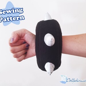Könnte beinhalten: Schwarzer Stoff-Handgelenk-Manschette mit drei silbernen Spikes. Die Manschette wird am Handgelenk einer Person getragen. Nähmuster.