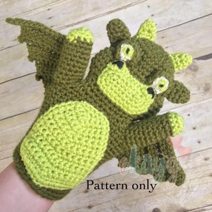 May include: Crocheted dragon hand puppet in shades of green. The puppet features a detailed dragon face with large eyes, a snout, and small horns. The text "Pattern only" is visible. The wings and claws are also visible.