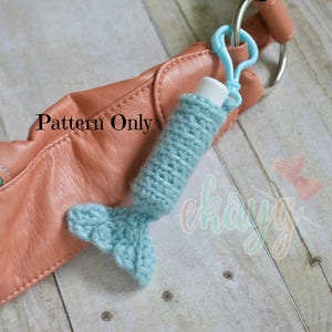 May include: A teal blue crocheted mermaid tail charm attached to a light blue keychain. The charm is attached to a brown leather purse.