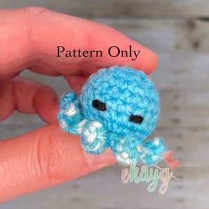 May include: A crocheted blue octopus with white accents. The octopus has black eyes and is being held by a hand. The text "Pattern Only" is visible in the image.