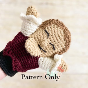 May include: Crocheted puppet hand warmer with a burgundy, black, and white color scheme. The puppet is a person with a brown face and closed eyes. The text "Pattern Only" is visible in the image.