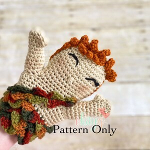 May include: Crocheted hand puppet with a brown body, orange hair, and a green, orange, and brown leaf skirt. The puppet is holding its arms up in the air. The text "Pattern Only" is visible in the image.
