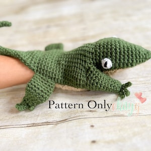 Puede incluir: Marioneta de gecko de crochet verde con ojos blancos. La marioneta está en la mano de una persona y el texto "Pattern Only" es visible debajo de la marioneta.