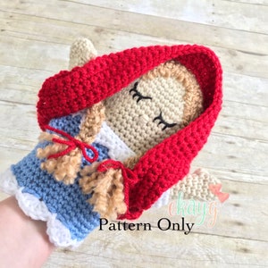 May include: Crochet pattern for a red hooded doll with blonde hair and a blue dress. The doll is wearing a red hooded cloak and has closed eyes. The pattern is for sale and the text "Pattern Only" is visible in the image.