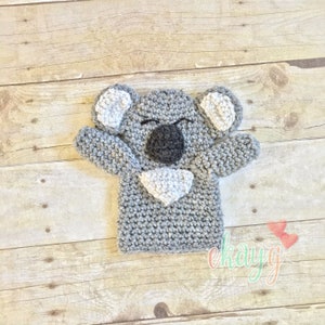 May include: Gray crocheted koala puppet with white ears and a black nose. The puppet is designed to fit on a hand.
