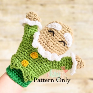 May include: Crocheted gingerbread person puppet with green and yellow clothing, white ruffle trim, and a smiling face. The puppet is attached to a green crocheted glove. "Pattern Only" is written below the puppet.