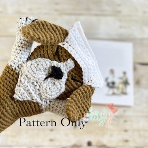 Può includere: Schema all'uncinetto per un amigurumi di cane marrone e bianco. Il cane indossa un cappello bianco all'uncinetto. Lo schema è disponibile per l'acquisto. Il testo "Pattern Only" è visibile nell'immagine.