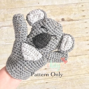 May include: A gray crocheted koala amigurumi toy with black eyes and white ears. The toy is being held by a hand. The text "Pattern Only" is visible in the image.