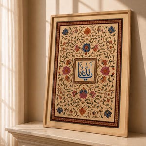 May include: A framed rectangular artwork featuring a central blue Arabic calligraphy inscription surrounded by an intricate floral pattern with pink, orange, and blue blossoms on a cream background, enclosed in a thin light-colored wooden frame.