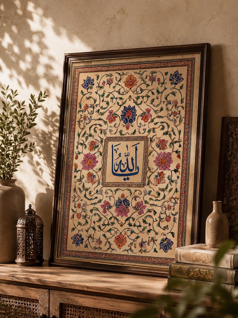 May include: A framed rectangular wall art piece featuring intricate floral patterns in shades of blue, pink, orange, and green surrounding a central square containing blue Arabic calligraphy on a light beige background with a dark brown frame.