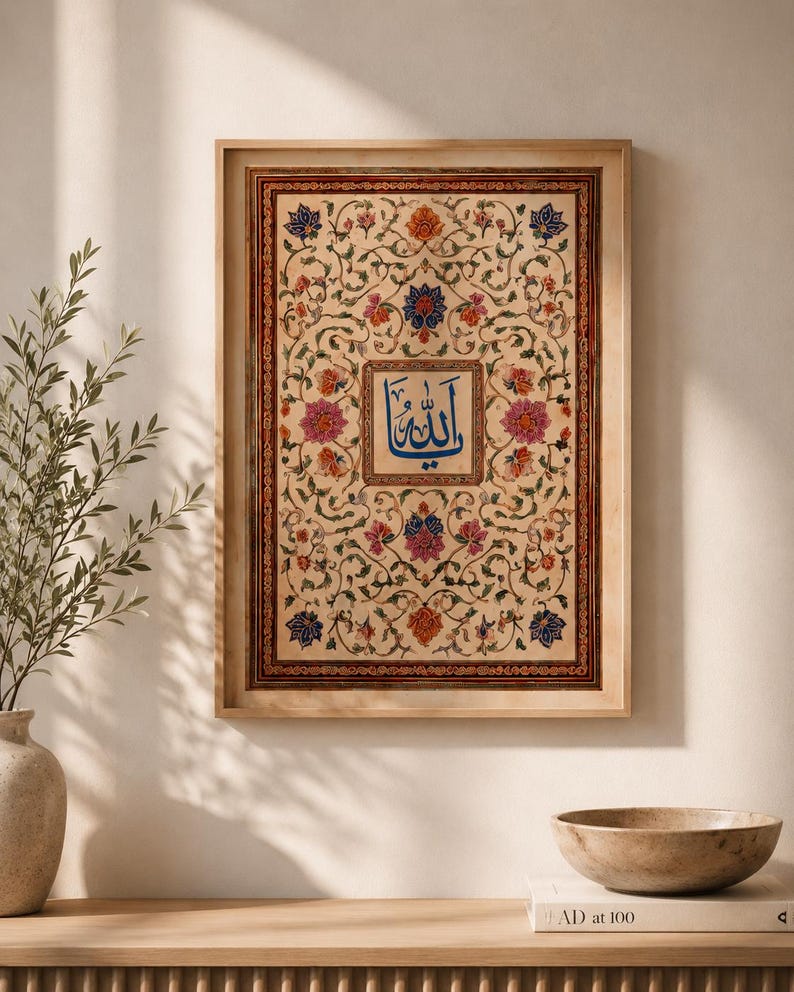May include: A rectangular framed wall art piece featuring intricate floral patterns in shades of pink, orange, and blue on a cream background. A central square contains blue Arabic calligraphy. The frame is a light-toned wood with a thin border.