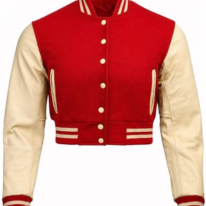 Pode incluir: Casaco universitário vermelho curto com mangas de couro creme. O casaco apresenta uma frente abotoada, punhos e gola canelados creme com riscas brancas e dois bolsos frontais. Um casaco clássico de inspiração atlética.