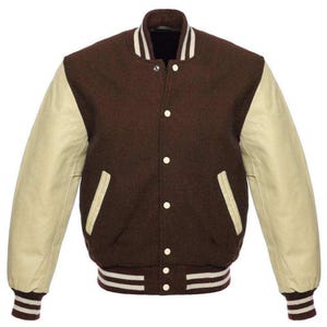 May include: A brown and cream varsity jacket with a button-up front. The jacket features cream-colored sleeves, a brown body, and white striped detailing on the collar, cuffs, and hem. The jacket has two front pockets and a classic, sporty design.