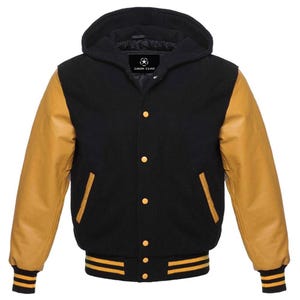 Könnte beinhalten: Eine schwarze Collegejacke mit beigen Ärmeln und Kapuze. Die Jacke verfügt über eine Knopfleiste mit goldfarbenen Druckknöpfen, zwei Seitentaschen mit beigem Rand sowie gerippte Bündchen und einen Saum mit schwarzen und beigen Streifen. Das Etikett zeigt SAIDA GEAR.
