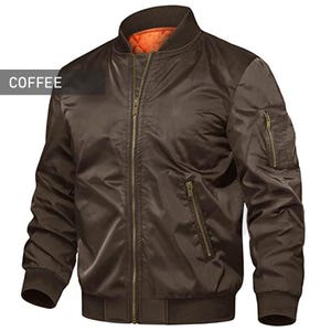 Pode incluir: Casaco bomber cor café com gola, punhos e bainha canelados. O casaco tem um fecho de correr completo, dois bolsos laterais e um bolso com fecho na manga esquerda. O forro interior é laranja. A palavra "COFFEE" está numa caixa branca.