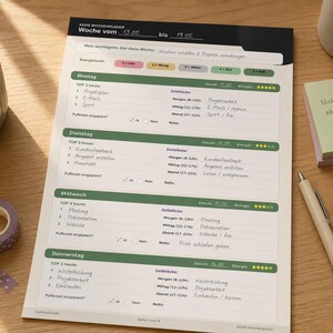 May include: A weekly planner with a black and green header, featuring sections for each day of the week. The planner includes space for tasks, time blocks, and notes. A succulent plant, pen, and sticky notes are also on the wooden desk.
