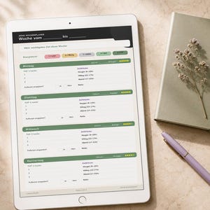 May include: A white tablet displaying a weekly planner with green and pink accents, a sage green notebook with a sprig of dried flowers, and a lavender pen. The planner is open to a page with German text.