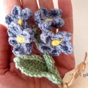 May include: A crocheted bouquet of blue flowers with yellow centers and green leaves. The flowers are tied together with twine and a small tag.