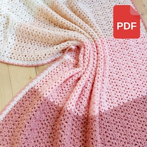 May include: A crocheted blanket with a gradient of pink, peach, and white. The blanket is folded in half and has a PDF label attached.