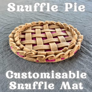 Op de afbeelding: Een Snuffle Pie-mat van vilt met een geweven bovenkant en een roze binnenkant. De mat heeft een gerimpelde rand en de tekst "Snuffle Pie" en "Customisable Snuffle Mat" in het wit.