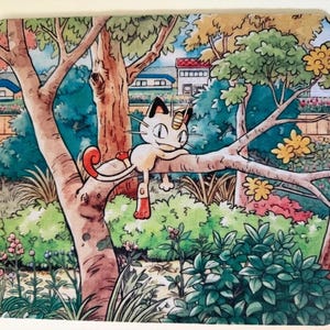 Op de afbeelding: Een rechthoekige muismat met een kleurrijke illustratie van een crèmekleurig katachtig wezen met een gouden munt op het voorhoofd, zittend op een boomtak in een weelderige tuin met groene struiken, bomen en een huis op de achtergrond.