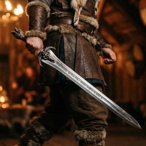 May include: A silver sword with a detailed dragon head hilt and engraved runes along the blade. The sword is held by a person wearing a brown leather and fur outfit, suggesting a historical or fantasy theme.