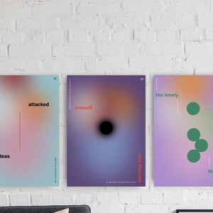 May include: Three framed art prints with abstract designs. The first print has a gradient of pink, blue, and orange with the words "attacked by ideas." The second print is purple with a black circle and the word "oneself." The third print is lavender with green circles and the words "the lonely the many."
