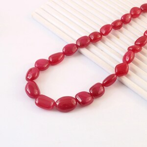 Può includere: Una collana di perline ovali rosso scuro lucido, disposte in una linea curva. Le perline hanno una finitura liscia e brillante e sono uniformi nel loro vibrante colore cremisi, creando una catena continua di componenti arrotondati.