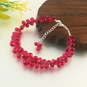 May include: A vibrant red gemstone bracelet. The bracelet features numerous teardrop-shaped, faceted red gemstones strung together. A silver chain and clasp secure the bracelet. The gemstones are arranged in a circular pattern.