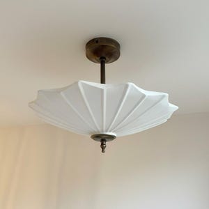 Può includere: Un lampadario bianco in stile Art Déco con un paralume scanalato a forma di ventaglio. L'apparecchio ha uno stelo color ottone e accenti decorativi. La luce è montata su un soffitto bianco.