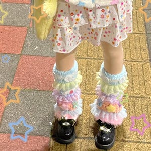 May include: A white fleece vest with pastel star patterns, a white skirt with a small colorful floral print, and layered pastel ruffled leg warmers in blue, yellow, pink, and purple, paired with black shoes and a yellow fuzzy bag.