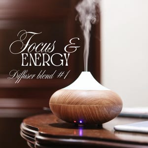 Könnte beinhalten: Ein Diffusor für ätherische Öle in Holzoptik mit weißem Oberteil, der einen Dampfstrahl abgibt. Der Text "Focus & ENERGY, Diffuser blend #1" ist in weißer Schrift dargestellt. Der Diffusor steht auf einer dunklen Holzoberfläche.